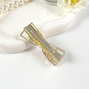 Detail view of the silver metal bow hair clip with a gold base and duckbill clamp