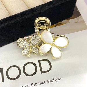 Macro shot of gold butterfly hair claw clip with rhinestones and white petals on a mood board