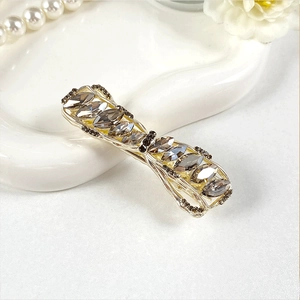 Close-up of an elegant gold alloy hair clip with grey crystals in a bow design