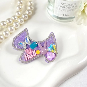 Détail d'une pince à cheveux nœud violet avec lettrage Hello et breloques mignonnes sur plateau