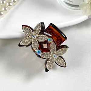 Detail view of flower hair claw clip with rhinestones and iridescent gems on white surface