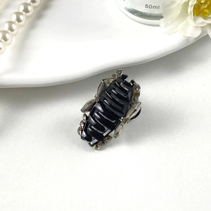 Détail d'une petite pince à cheveux noire à strass gris sur une assiette blanche élégante