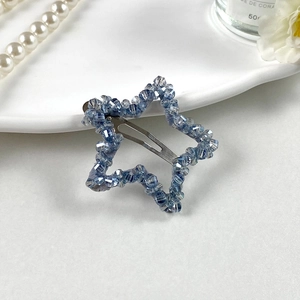 Détail d'une pince à cheveux étoile en cristal bleu sur fond blanc avec des perles