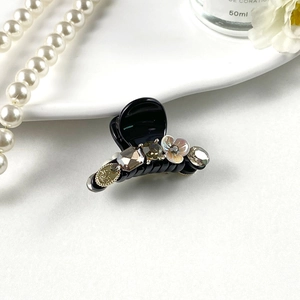 Detailed shot of black hair claw with shell flower and rhinestones on porcelain