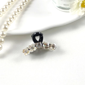 Detail of small black hair claw clip with rhinestones and white flowers on a desk