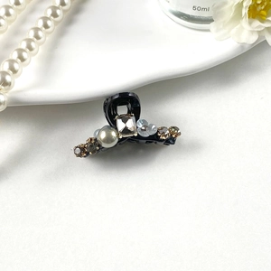 Detail of elegant black hair claw clip with champagne crystal, pearl, and blue flower