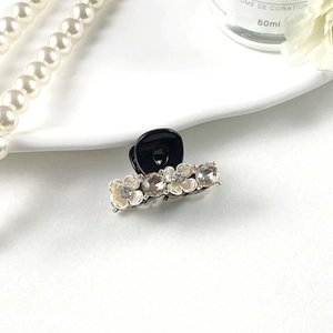 Detail of mini hair claw clip featuring white flowers and rhinestones on black base