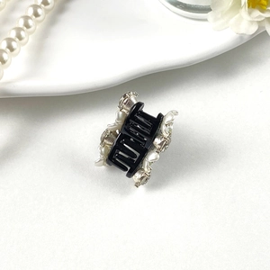 Detail of mini hair claw clip featuring white pearls and sparkling rhinestones on black resin