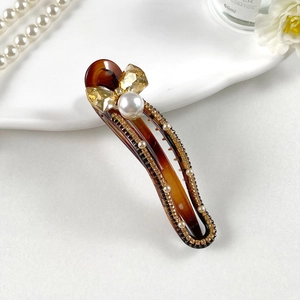 Detailed close-up of tortoise shell hair clip with golden crystal bow and pearl accents