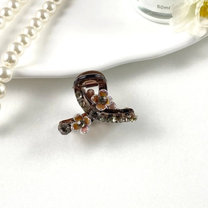 Detailed view of a brown pearl rhinestone hair clip with floral accents and soft lighting