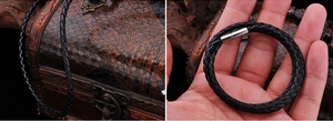 Detail of black braided leather necklace with a silver magnetic screw clasp on wood background