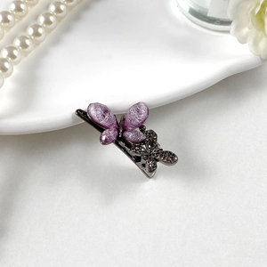 Dettaglio del fermaglio a farfalla scuro con texture in seta viola e strass luccicanti