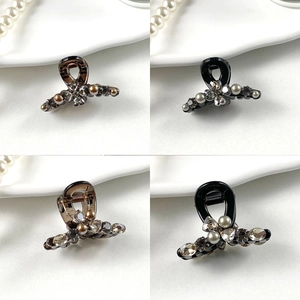 Detailed view of mini hair clips with rhinestones and pearls on a white porcelain plate