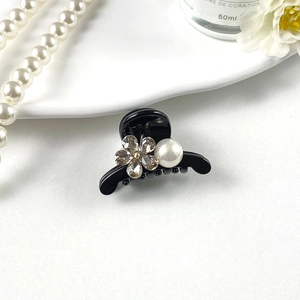 Detail of mini black hair claw clip featuring sparkling rhinestones and a white pearl accent