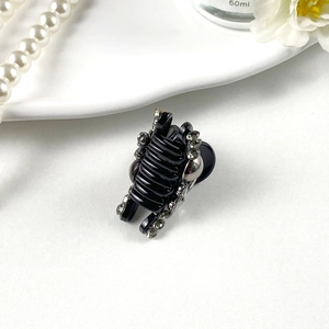 Detailed view of mini black hair claw clip with sparkling grey rhinestones on a tray
