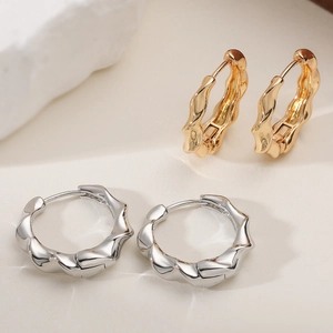 Polished wavy gold and silver hoop earrings set on a minimalist textured surface