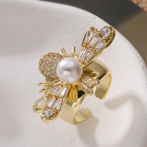 Macro shot of gold bee ring detailing white pearl and zircon wings on polished metal