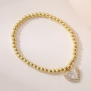 Gros plan du bracelet à perles dorées 18K avec pendentif cœur en nacre et zircons