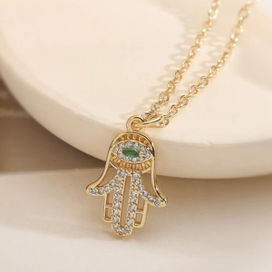 Collier Main de Fatma doré avec pierre de zircon verte sur support en pierre blanche