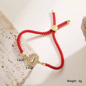 Detail of red rope bracelet with 18K gold Virgin Mary pendant and zircons on stone background