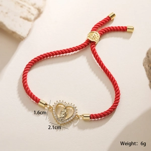 Detailed macro view of heart Virgin Mary pendant with cubic zirconia on red rope bracelet