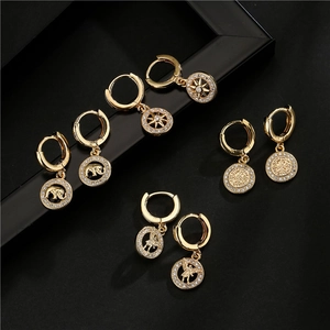 Detalle de pendientes de aro bañados en oro de 18K con dijes de circón sobre fondo negro