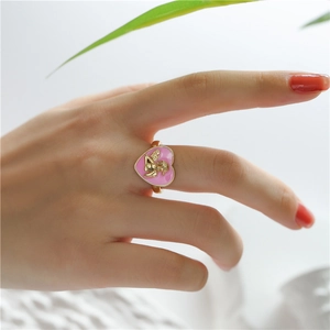 Detail of a gold heart ring with pink enamel and 3D cupid relief worn on finger