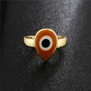 Golden teardrop open ring featuring evil eye enamel pattern on a black textured background