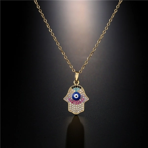 Collier Hamsa doré avec pendentif œil maléfique en zircon coloré sur fond sombre et reflétant