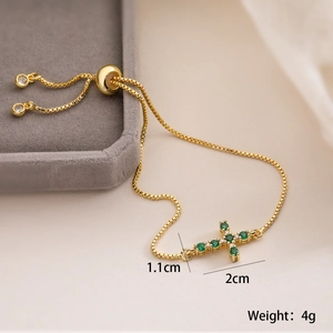 Macro view of 18K gold plated cross bracelet with green zircon and adjustable slider clasp