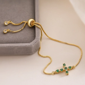 Detail of adjustable 18K gold cross bracelet with green zircons on velvet box
