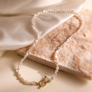 Elegant Baroque pearl necklace with golden textured toggle clasp on white silk background