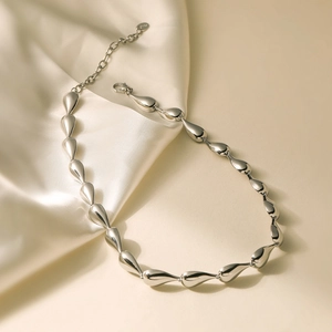 Polished silver stainless steel teardrop bead necklace on silk fabric background