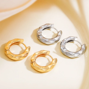 Golden and silver wave textured geometric hoop earrings on a minimalist cream ceramic tray