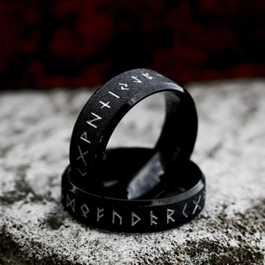 Anillos minimalistas de acero inoxidable negro con runas vikingas sobre fondo de piedra gris