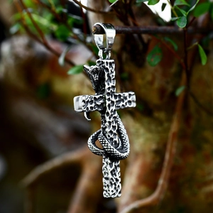 Macro detail of gothic stainless steel cross pendant with a coiled snake on a branch