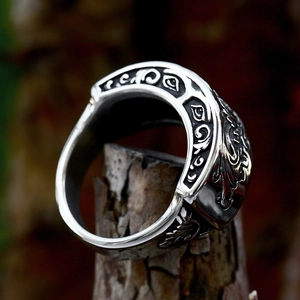 Vintage stainless steel ring with intricate floral carvings on rustic wood background