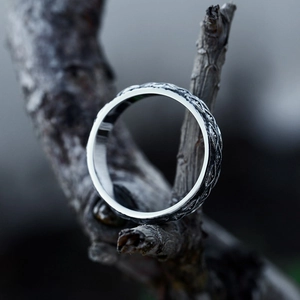 Macro shot of vintage stainless steel ring with intricate vine engravings on dry wood