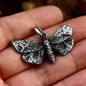 Macro detail of a vintage stainless steel moth pendant with gothic embossed wing textures