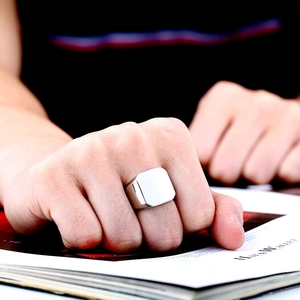 Close-up of polished silver square signet ring for men on finger with magazine background