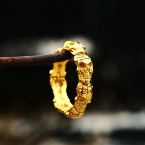 Macro shot of gold-plated skull ring hanging on rusty wire with dark blurred background