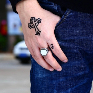Gothic cross tattoo sticker and silver hexagonal ring on hand over denim pocket