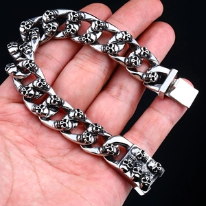 Bracelet tête de mort punk pour homme en acier inoxydable poli tenu dans la main sur fond noir