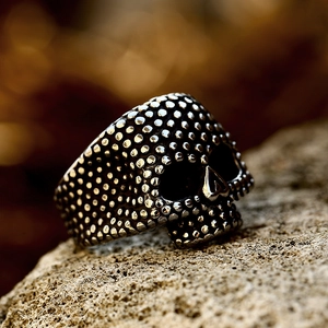 Punk style stainless steel skull ring with rivet texture on a natural rock background