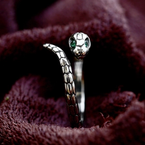Macro shot of silver snake ring featuring green gemstone eyes and detailed scale texture