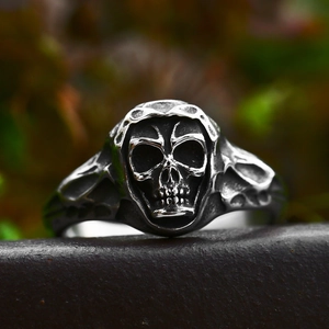 Gothic punk hooded skull ring in vintage stainless steel finish on a dark rock base