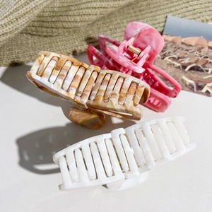 Close-up of three marble pattern bow claw clips in pink, amber, and white colors