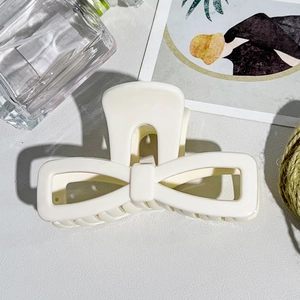 Detail view of large cream bow hair claw clip styled with decorative background props