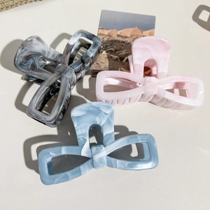 Three large marble pattern bow hair claws in grey pink and blue colors on a textured background