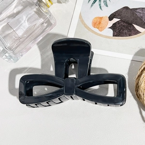 Close-up of a large black glossy bow hair claw clip on a textured white surface